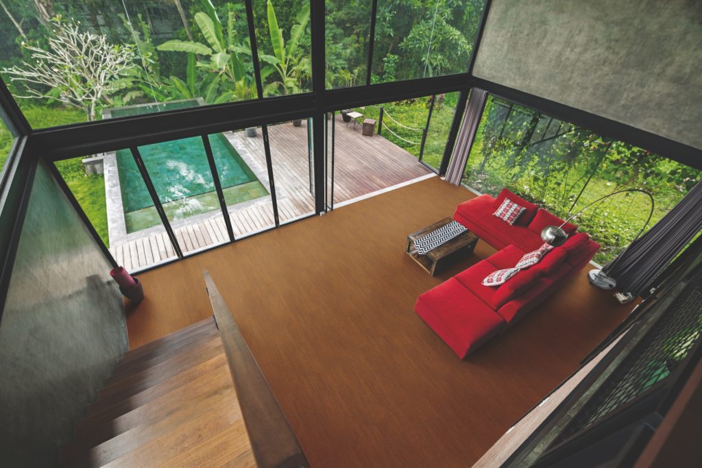 Modern minimalist living room with red couch in contemporary design house with glass facade surrounded by lush tropical garden with pool