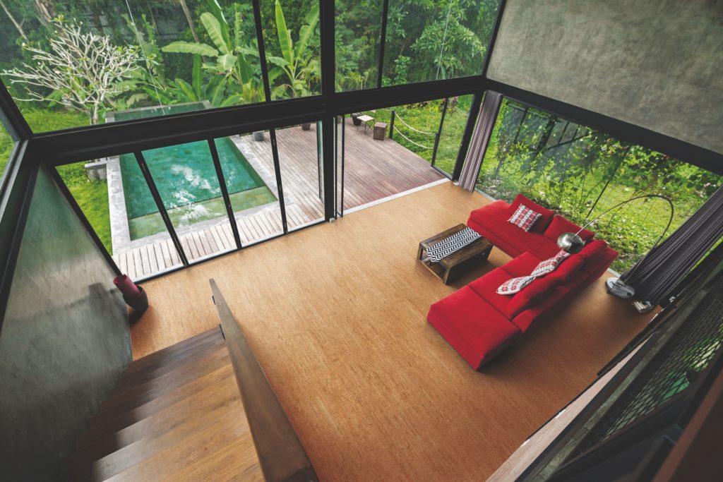 Modern minimalist living room with red couch in contemporary design house with glass facade surrounded by lush tropical garden with pool